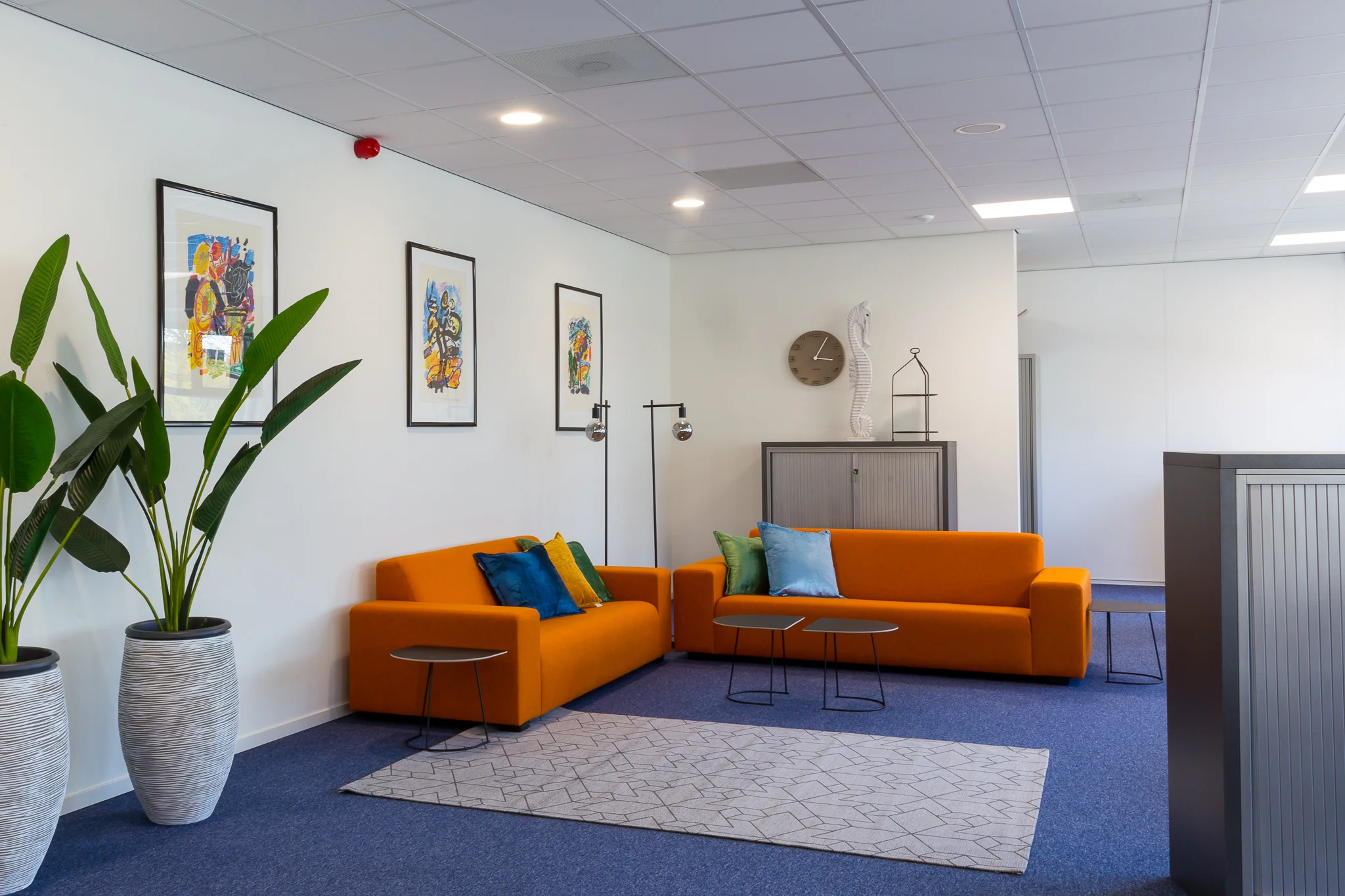 Moderne wachtruimte met oranje banken, kleurrijke kussens, planten en kunst aan de muur aan de Niels Bohrweg.